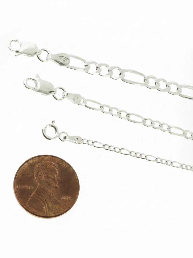 Close-up of a silver Figaro link anklet on a person's ankle against a blurred, minimalist background.
